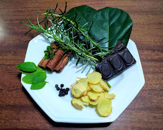 Ingredientes para fazer o Chá da Naoli. Contém folha de abacate, chocolate amargo, pimenta do reino, manjericão, paus de canela e alecrim.